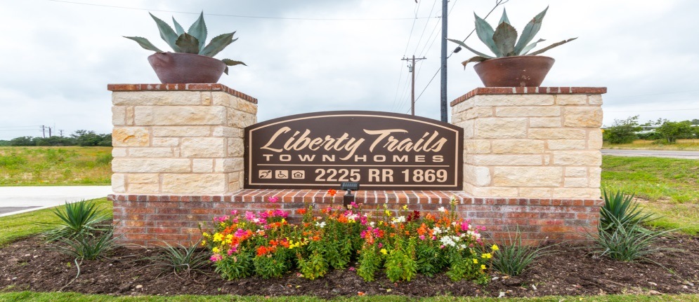 A sign for Liberty Trails Townhomes with a brick pillar and a plant on top.
